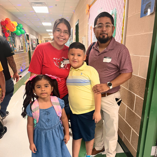 A happy family poses in a school hallway during an event. The warm atmosphere and colorful decorations indicate a back-to-school theme.