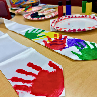 A creative art project featuring a white tie decorated with colorful handprints on a table with paint supplies. The scene evokes a playful and artistic mood.
