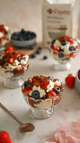 A delightful berry dessert with strawberries and blueberries served in glass bowls, topped with cream and chocolate crumbles. The setting is warm and inviting, suggesting a sweet treat ready to be enjoyed.