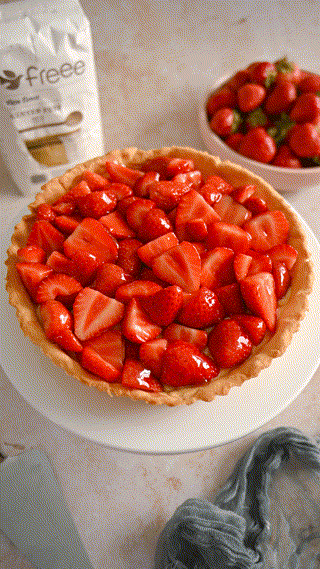 A vibrant strawberry tart on a white stand surrounded by fresh strawberries and baking ingredients. The scene exudes a warm and inviting culinary atmosphere.