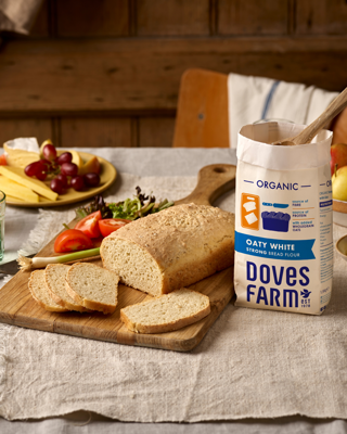 A rustic setup showcasing freshly baked bread and a bag of organic flour on a wooden table. The scene creates a warm and inviting atmosphere.