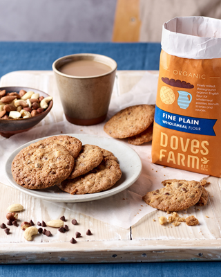 A cozy display of homemade cookies on a plate alongside a bag of organic wholemeal flour and a cup of coffee. A warm, inviting atmosphere for baking enthusiasts.