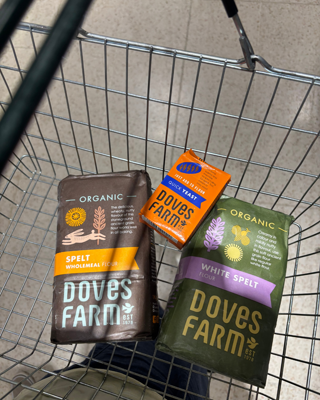 A shopping basket containing Doves Farm organic spelt flour and quick yeast, showcasing baking essentials in a store setting.