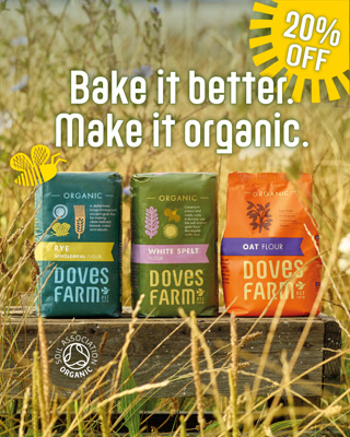 An advertisement for Doves Farm organic flours featuring three colorful packages on a wooden plank in a wheat field, promoting a 20% discount. The mood is natural and uplifting.