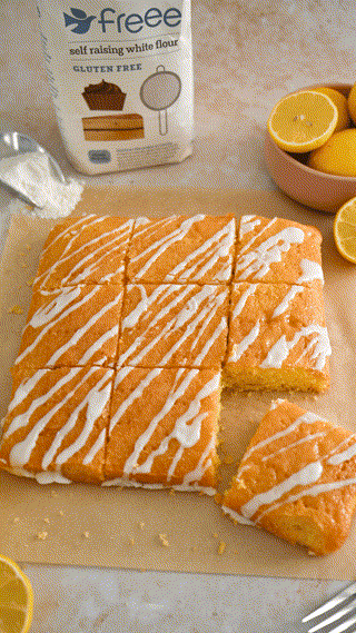 Slices of a gluten-free lemon drizzle cake with icing, displayed alongside a package of self-raising flour and fresh lemons. The scene is bright and inviting.