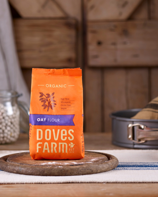 A bag of organic oat flour from Doves Farm placed on a wooden surface, with kitchen items in the background. The scene exudes a rustic and wholesome vibe.
